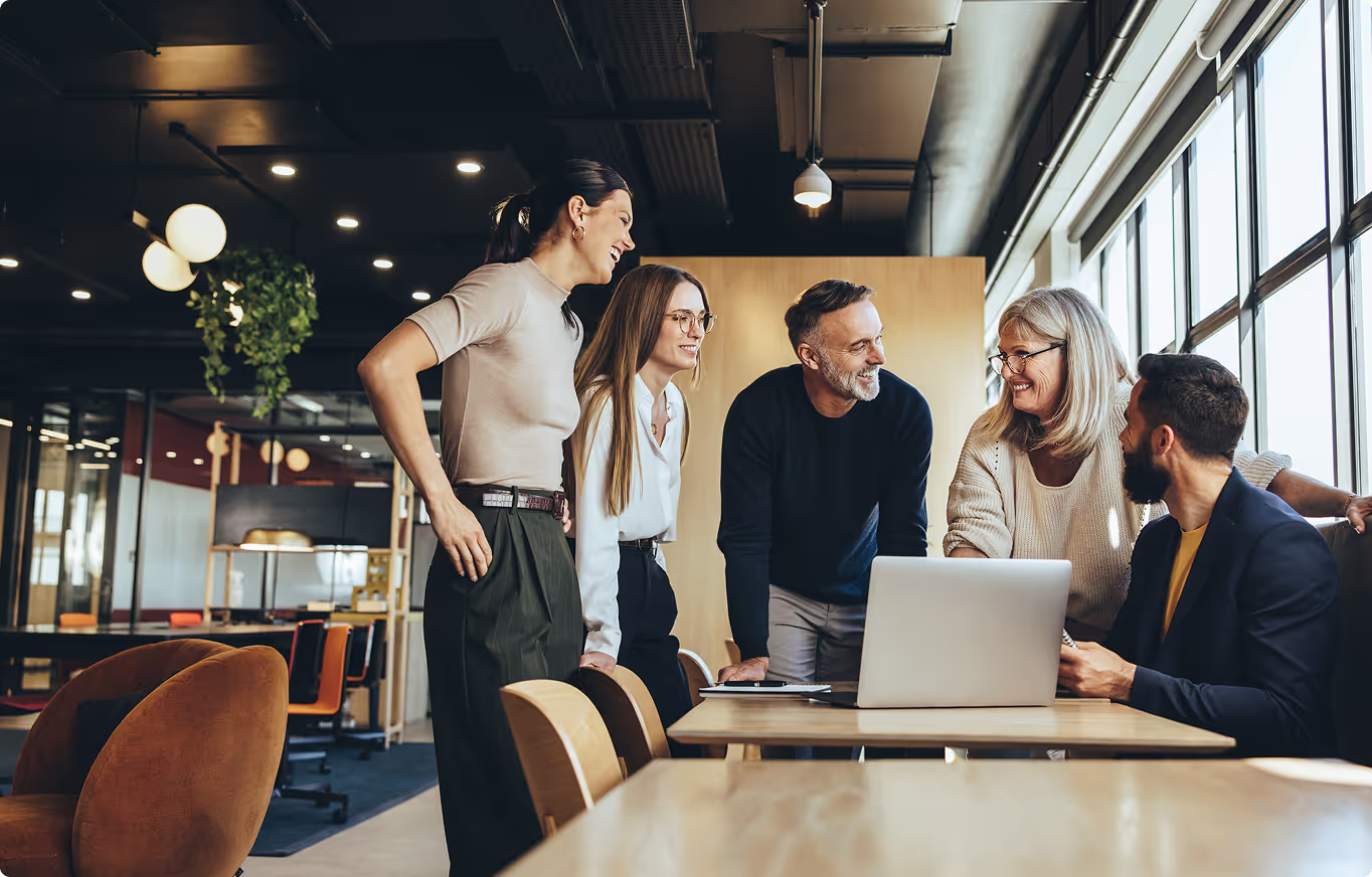 A group of people are gathered around a table with a laptop.